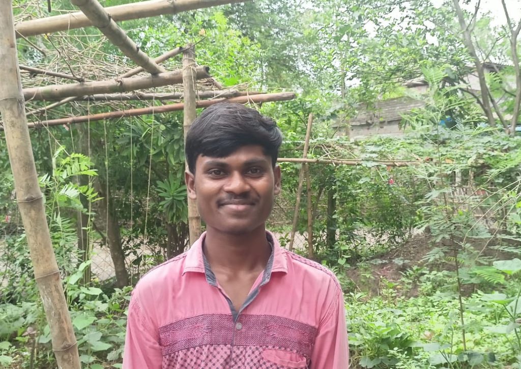 Sajal is standing infront of garden wearing his pink shirt and smiling.